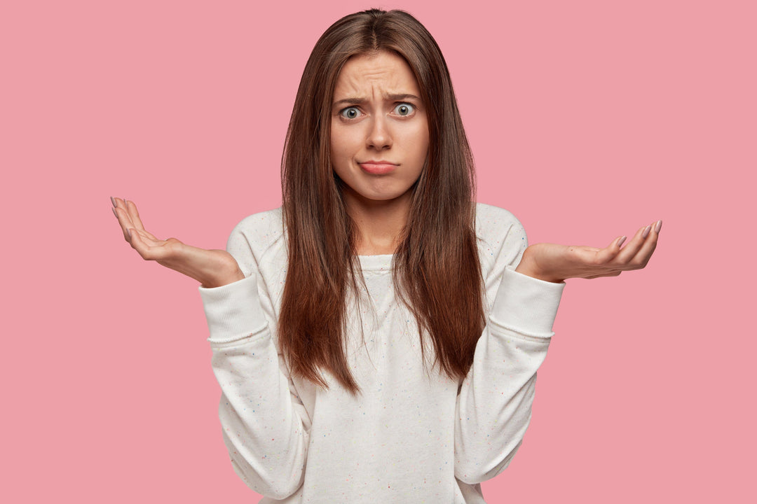 Woman looking confused by holding hands aloft against a pink background
