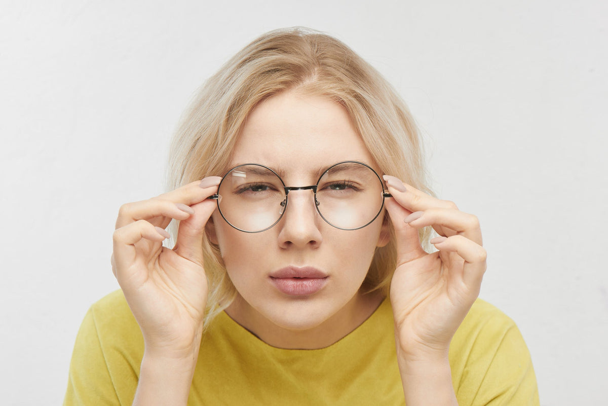 Woman squinting while adjusting round glasses