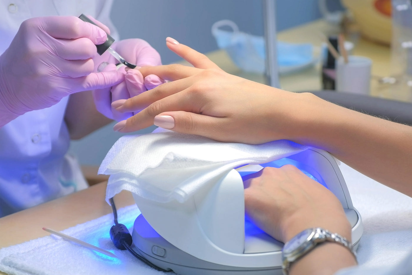 Woman with hand in UV lamp receiving manicure with other hand.