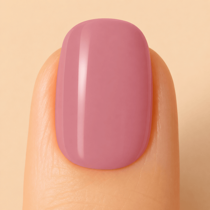 A close-up of a fingernail painted with a smooth, glossy dusty mauve pink polish, set against a solid light beige background.