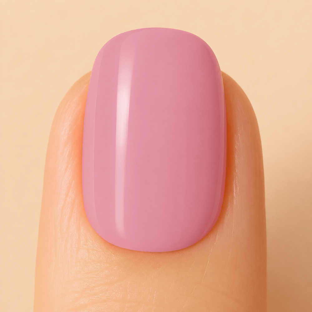 A close-up of a fingernail with a smooth, glossy, rounded square shape painted in a soft dusty pink color, set against a solid light beige background.