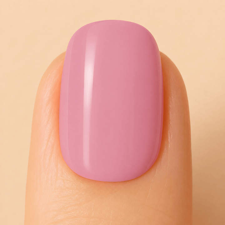A close-up of a fingernail with a smooth, glossy, rounded square shape painted in a soft dusty pink color, set against a solid light beige background.