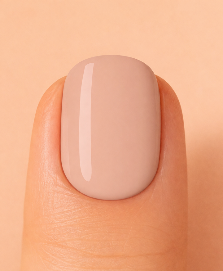 Close-up of a finger with a beige nail on a matching peach background
